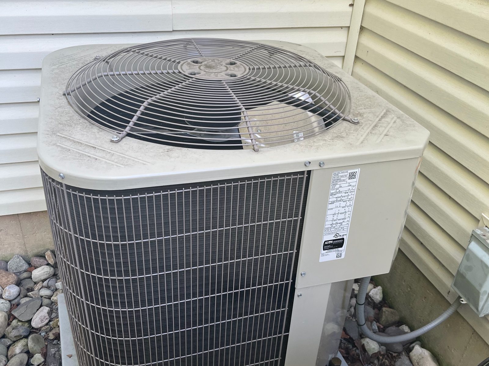 Central air conditioning condenser on a stone pad beside a house