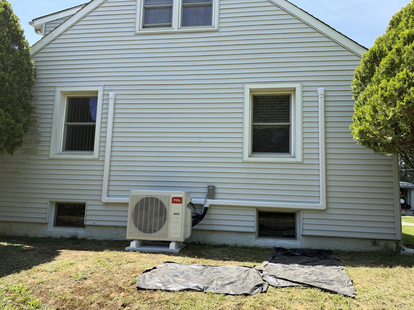 Ductless mini-split outdoor unit beside a gray-sided house, with white line-set covers