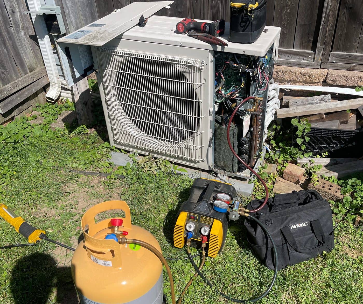 Ductless outdoor unit opened for repair, with gauges and a recovery machine