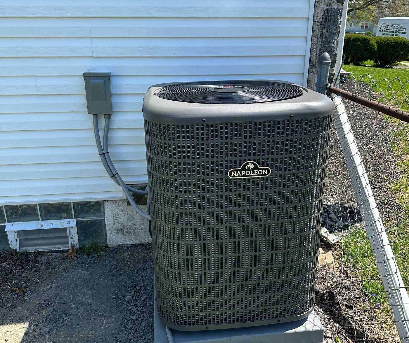 Central air conditioner condenser on a pad beside a white-sided house, with a C&L van in the background