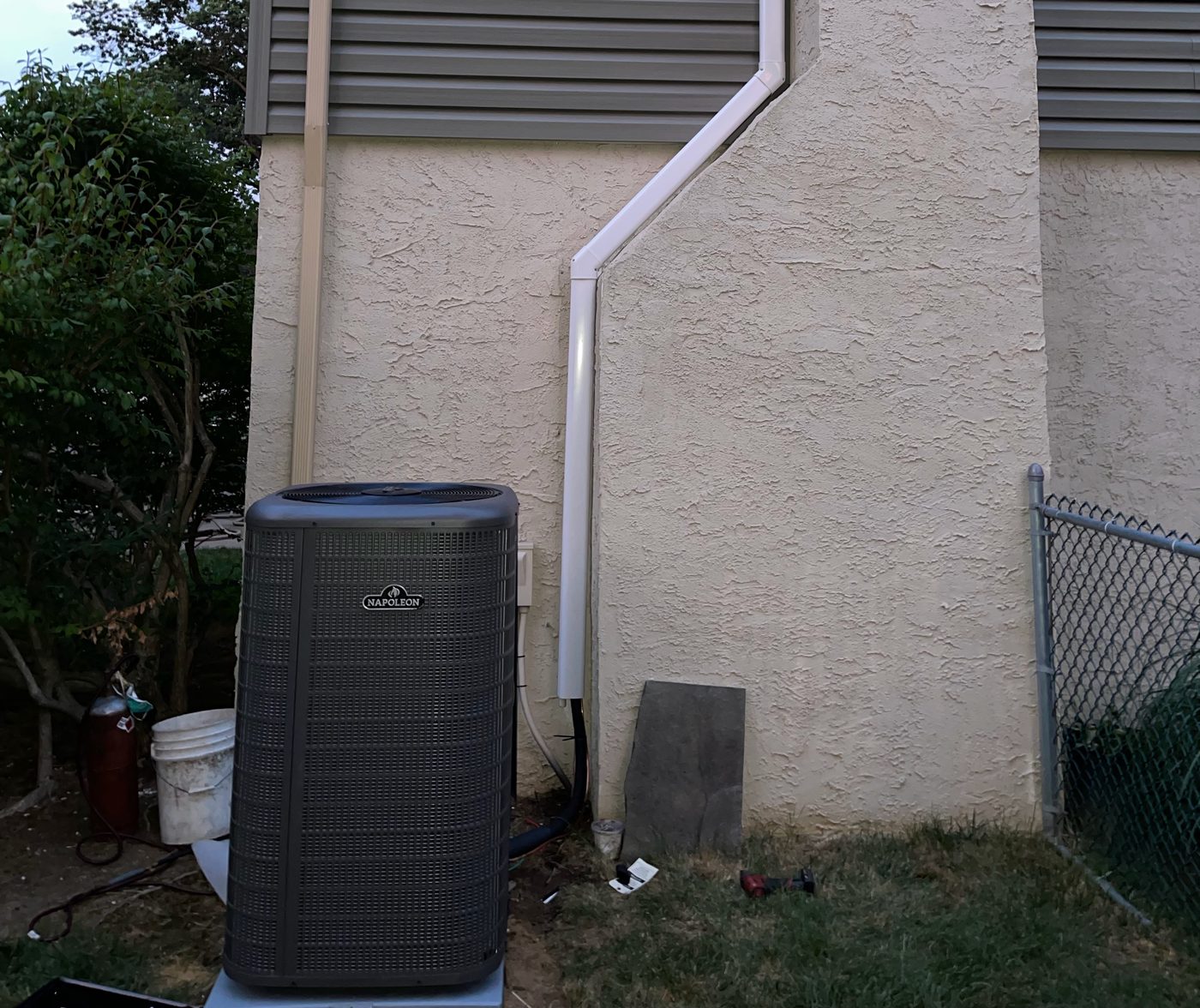 Central air conditioner condenser beside a stucco wall with a white line-set cover