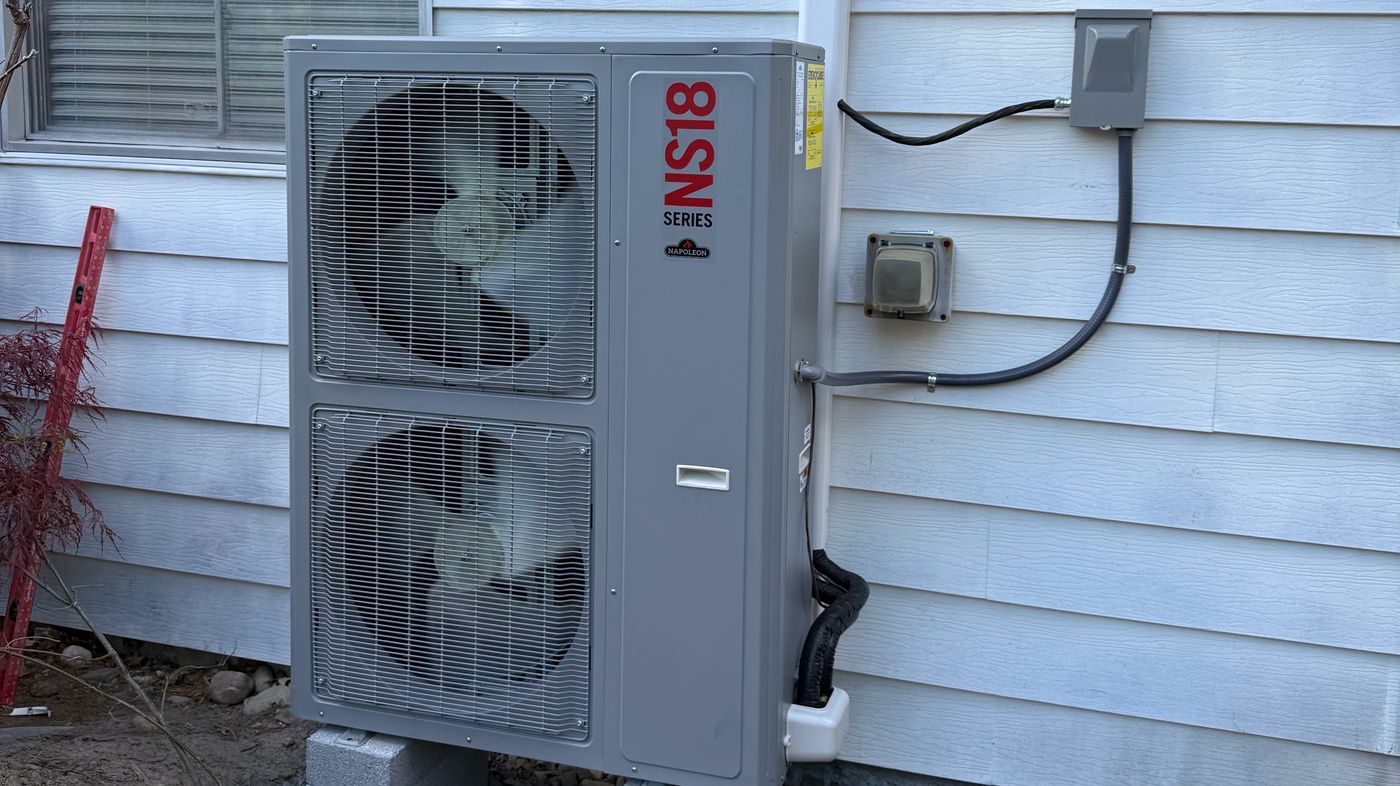 Heat pump outdoor unit on concrete blocks beside a white-sided house