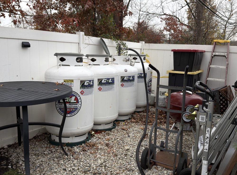 A row of C&L-labeled propane cylinders along a backyard fence