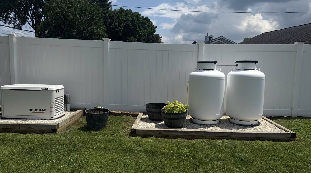 Two white residential propane tanks on a gravel pad beside a standby generator
