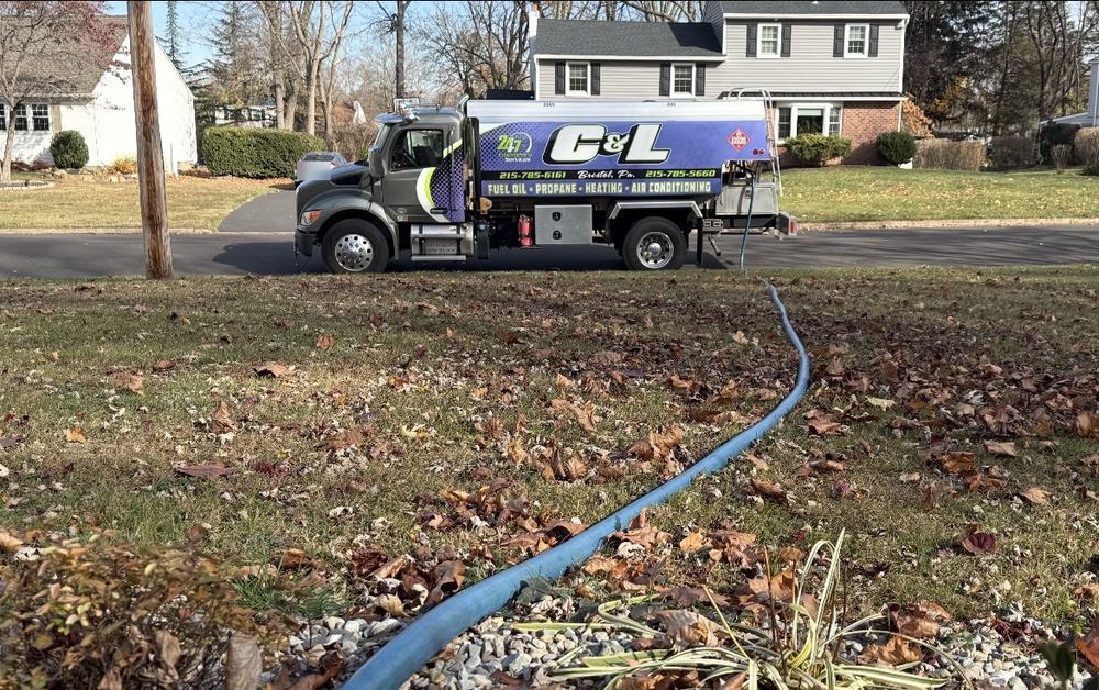 C&L Fuel heating oil delivery truck across the street, with its blue delivery hose running over a leafy lawn
