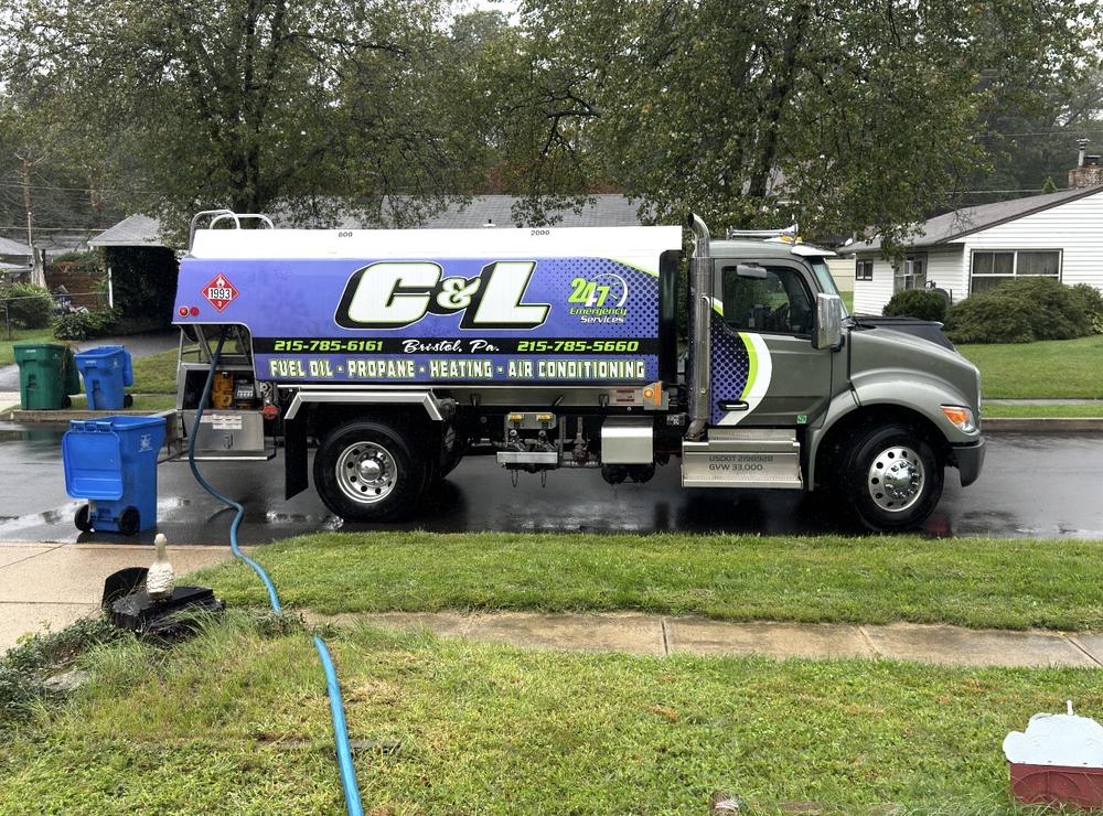 C&L Fuel heating oil delivery truck at the curb on a rainy day, with its hose run across the lawn to the house