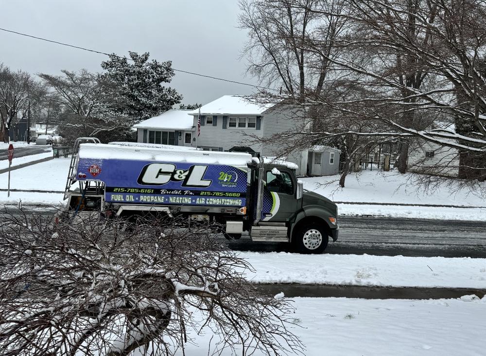 C&L Fuel heating oil delivery truck on a snowy street, seen past snow-covered branches