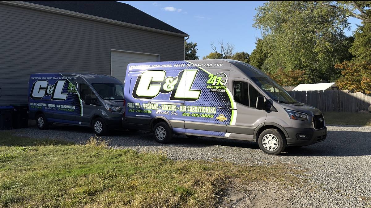 Two C&L Fuel service vans parked on gravel beside a garage