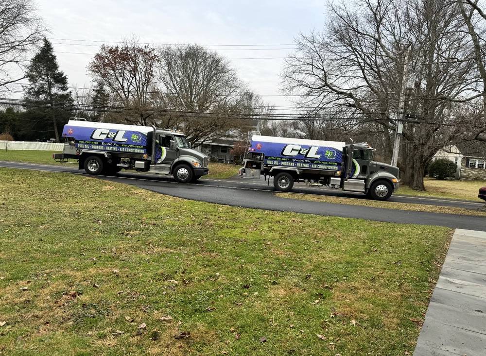 Two C&L Fuel heating oil delivery trucks on a road beside a grassy yard