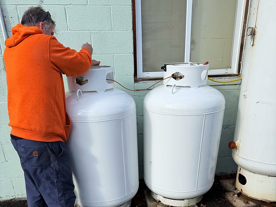 Technician checking two white residential propane tanks beside a house