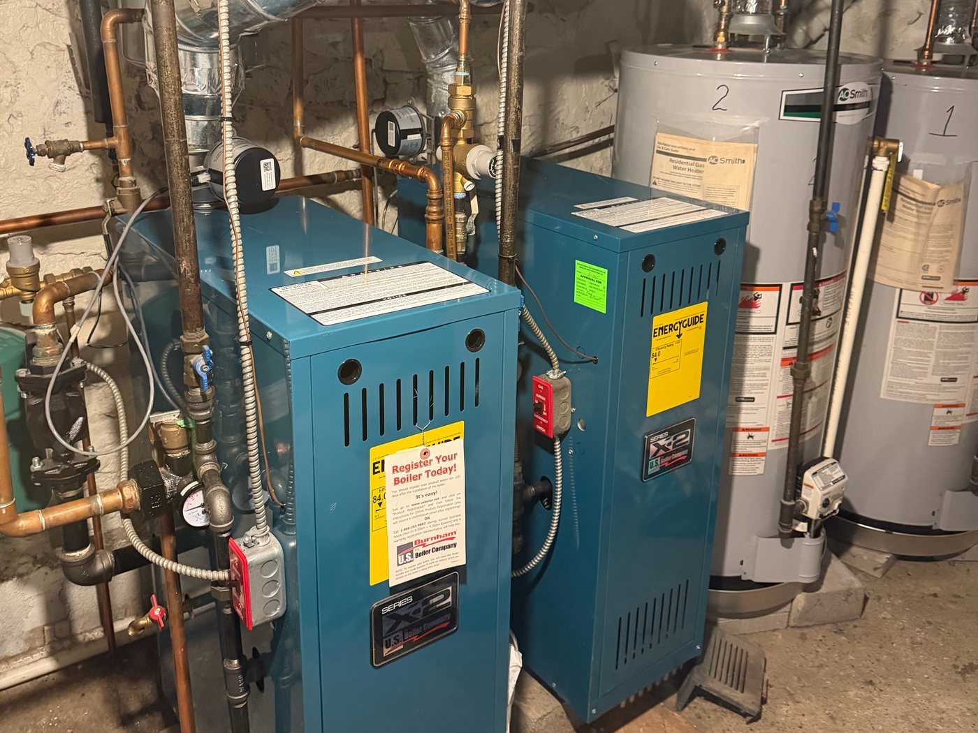 Two blue boilers and two water heaters in a basement
