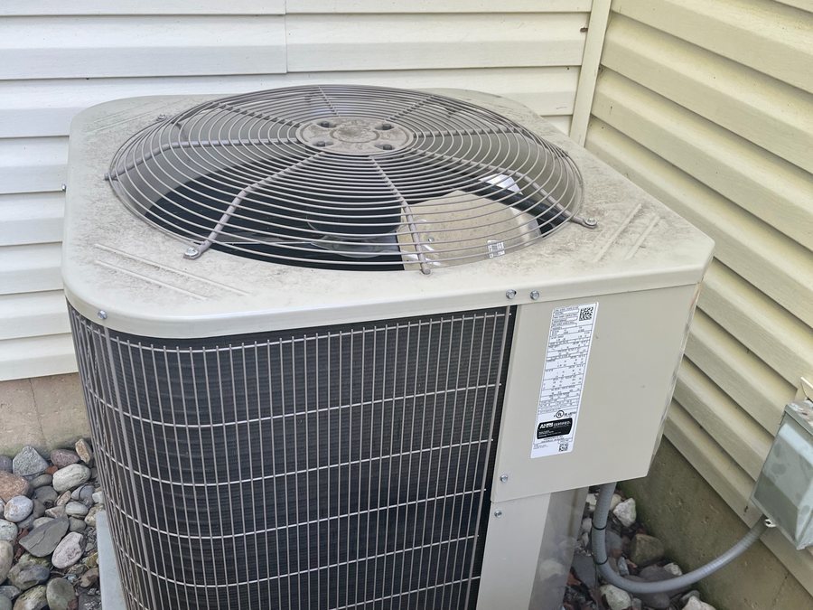 Air conditioner condenser beside siding, on a stone bed