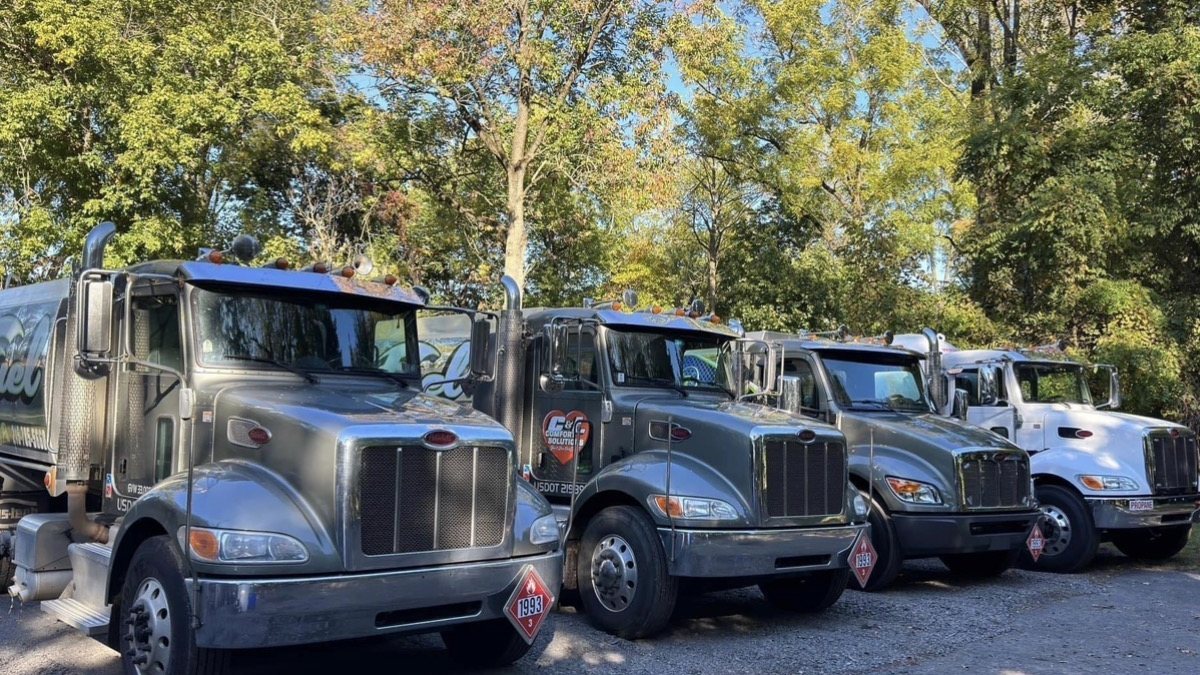 Four C&L Fuel delivery trucks parked in a row under autumn trees