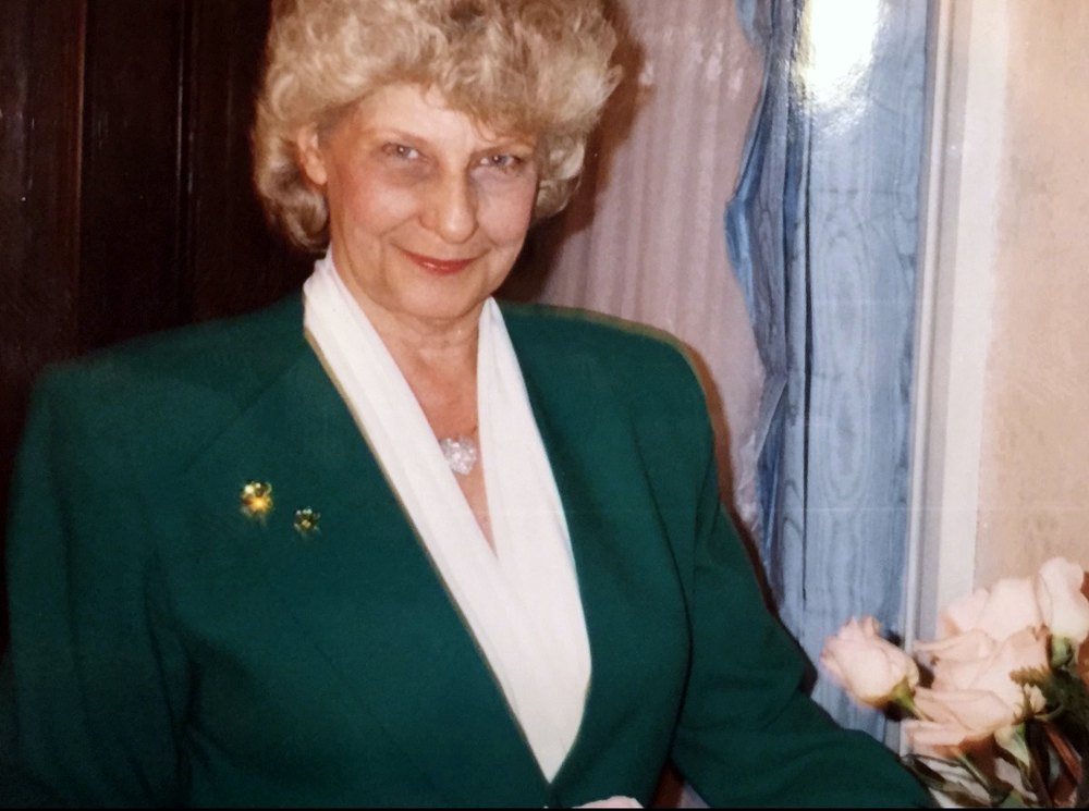 Susan smiling in a green blazer beside a vase of pink roses
