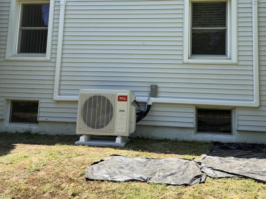 Ductless heat pump outdoor unit with a line set cover on the side of a house