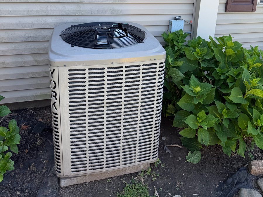 Heat pump outdoor unit beside a house with hydrangeas
